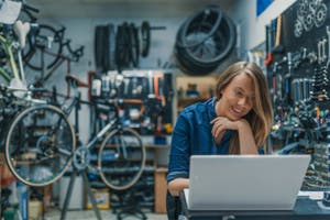 Bike mechanic working on a laptop in a workshop, engaged in creative tasks or business management.