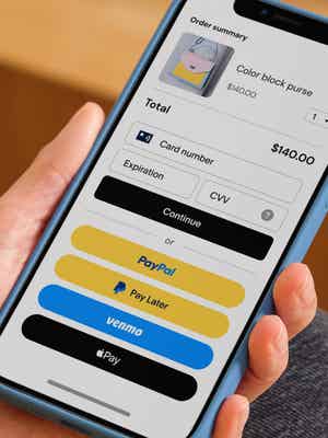 Person holding mobile phone showing checkout screen with payment options including debit/credit card, PayPal, Pay Later, Venmo, and Apple Pay.